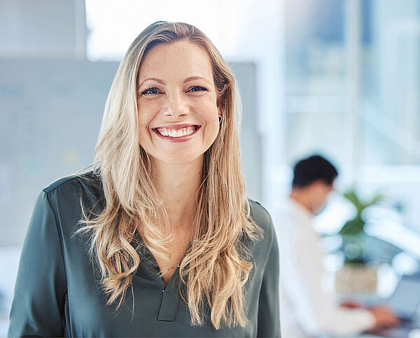 Lächelnde Mitarbeiterin der Verwaltung mit langen, blonden Haaren in einem hellen Büro.